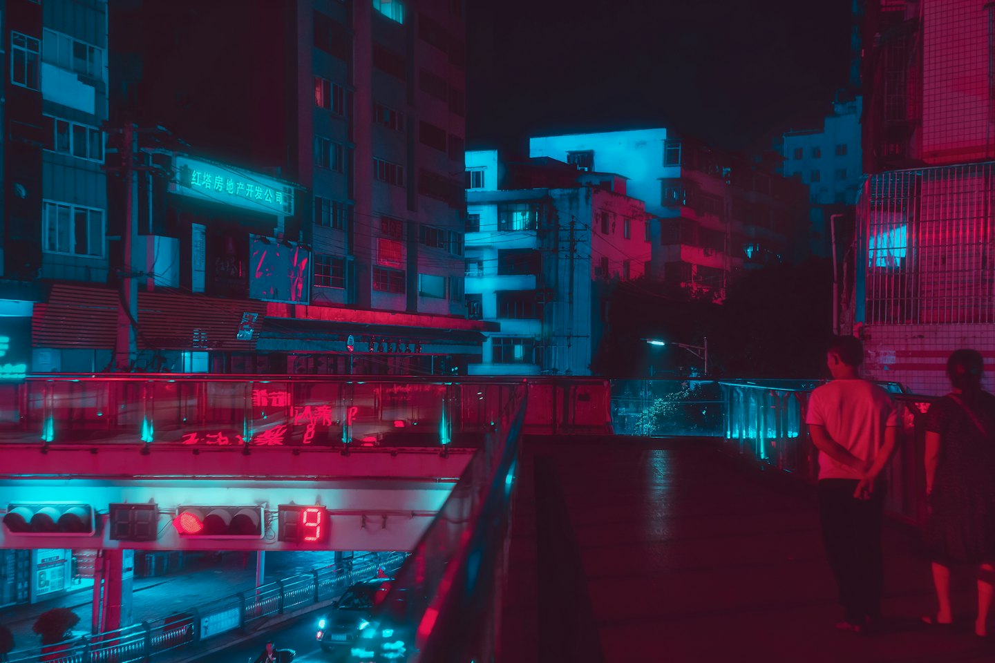 Two people stand on a glowing urban walkway overlooking city traffic.