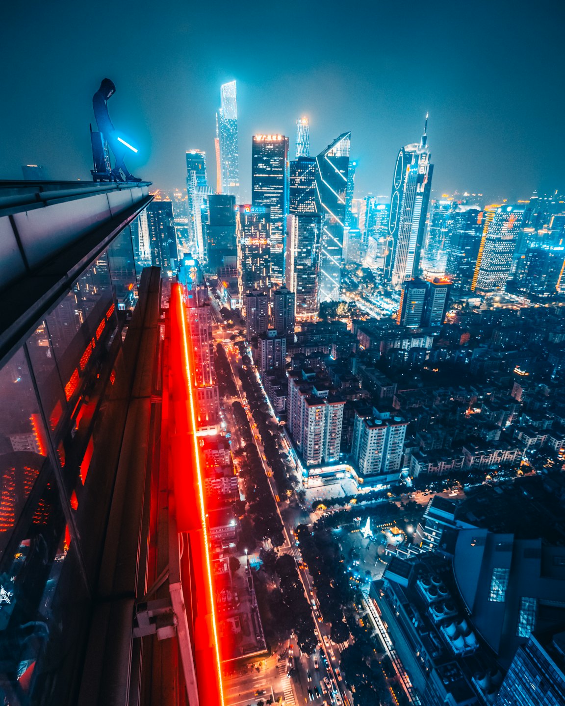 Person standing on a skyscraper edge holding a blue light.